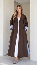 Front view of model wearing a brown maxi trench coat with striped turn-up cuffs over a white dress