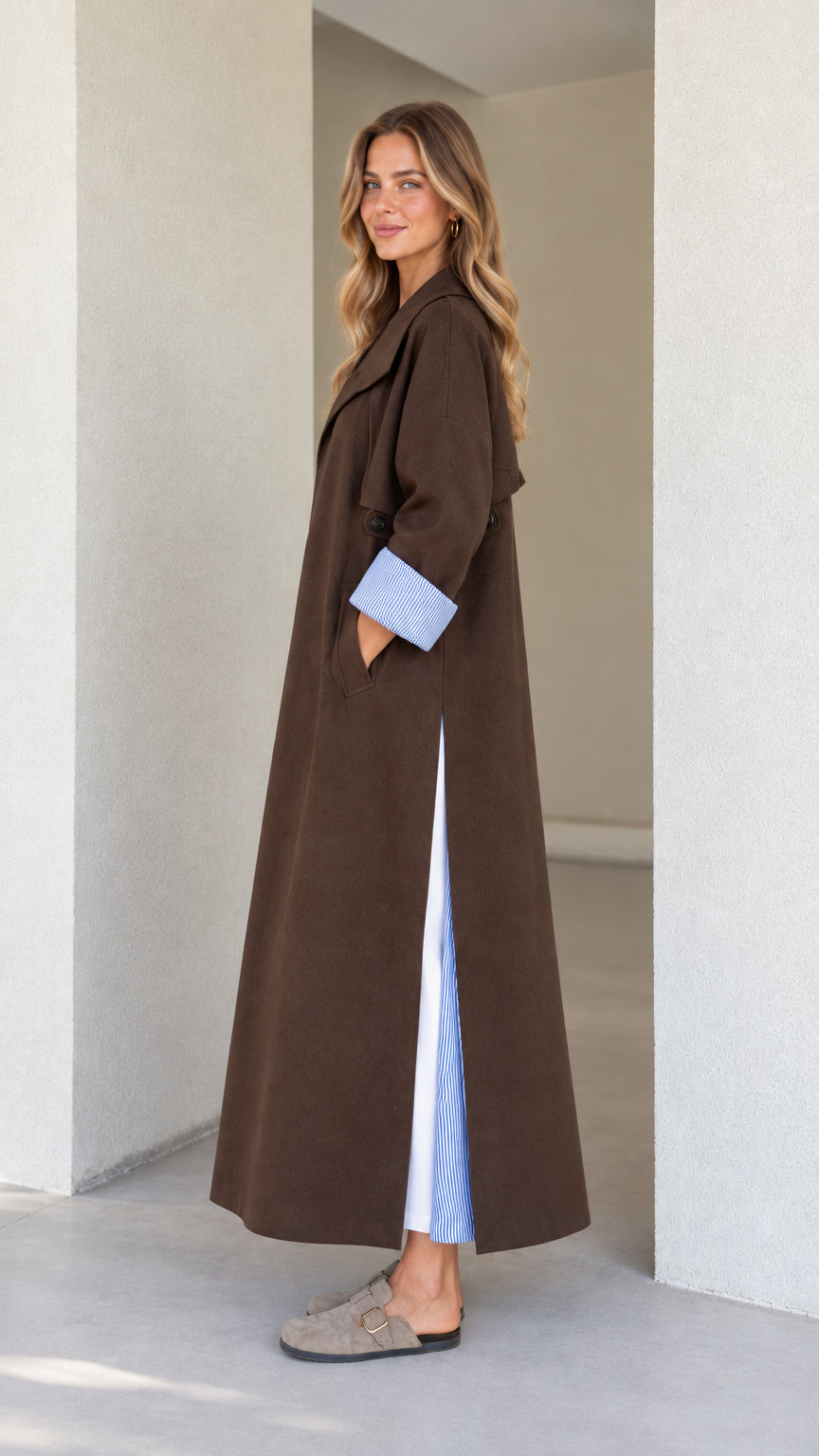 Side profile of model wearing the long brown duster coat showing the side slit with striped contrast